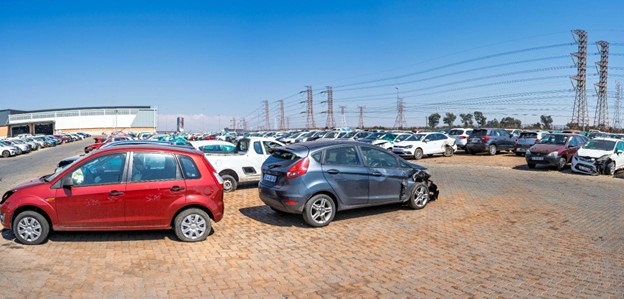 Wide outdoor shot of the massive sell your damaged car salvage yard under a bright blue sky.