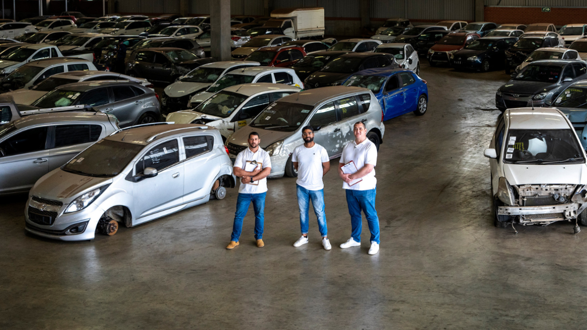 Three vehicle salvage specialists standing inside a warehouse filled with damaged cars.